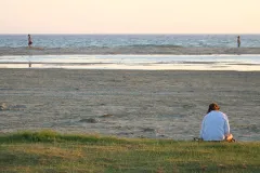 A woman sits on the beach reading a book. 