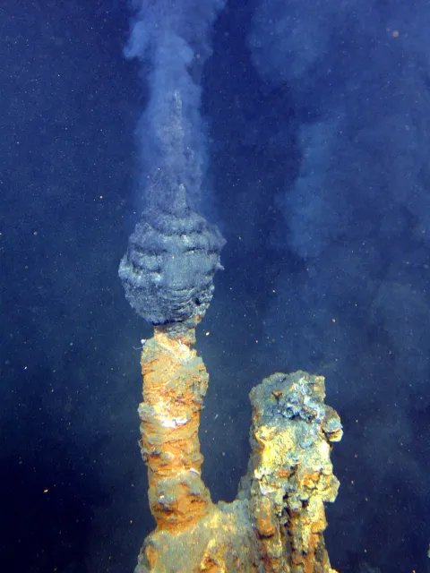 Dark smoke coming out of two vertical vents on the seafloor.